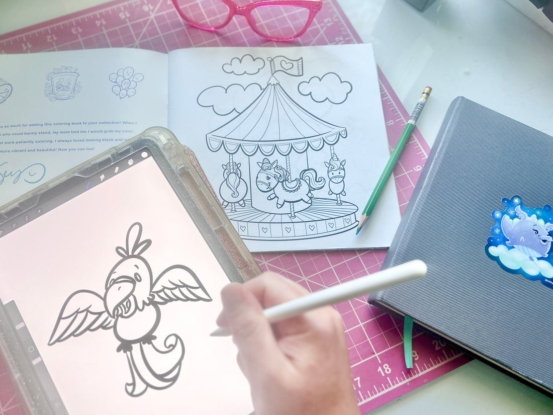 Artist drawing a parrot on ipad, surrounded by an open coloring book featuring a carosel, glasses, pencil, and a sketchbook with a dragon sticker.
