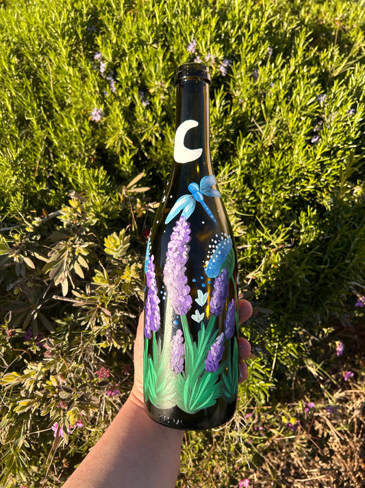 Photo showing wine bottle painted with a blue dragonfly and lavender flowers under the moonlight