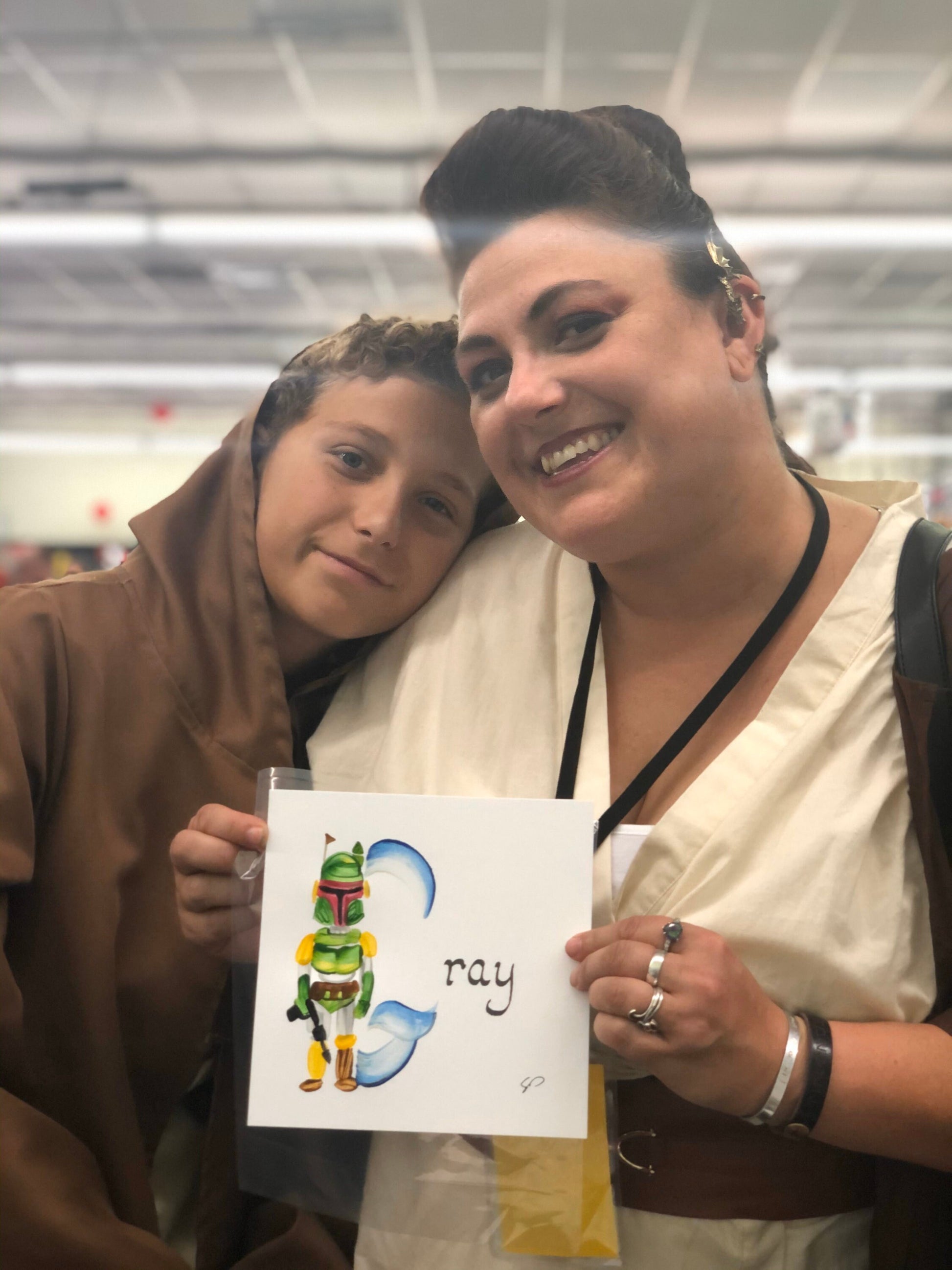 Mother & son holding up their new family name painting featuring a galaxy hunter with the name "Gray." Taken at Bakersfield Comic Con.